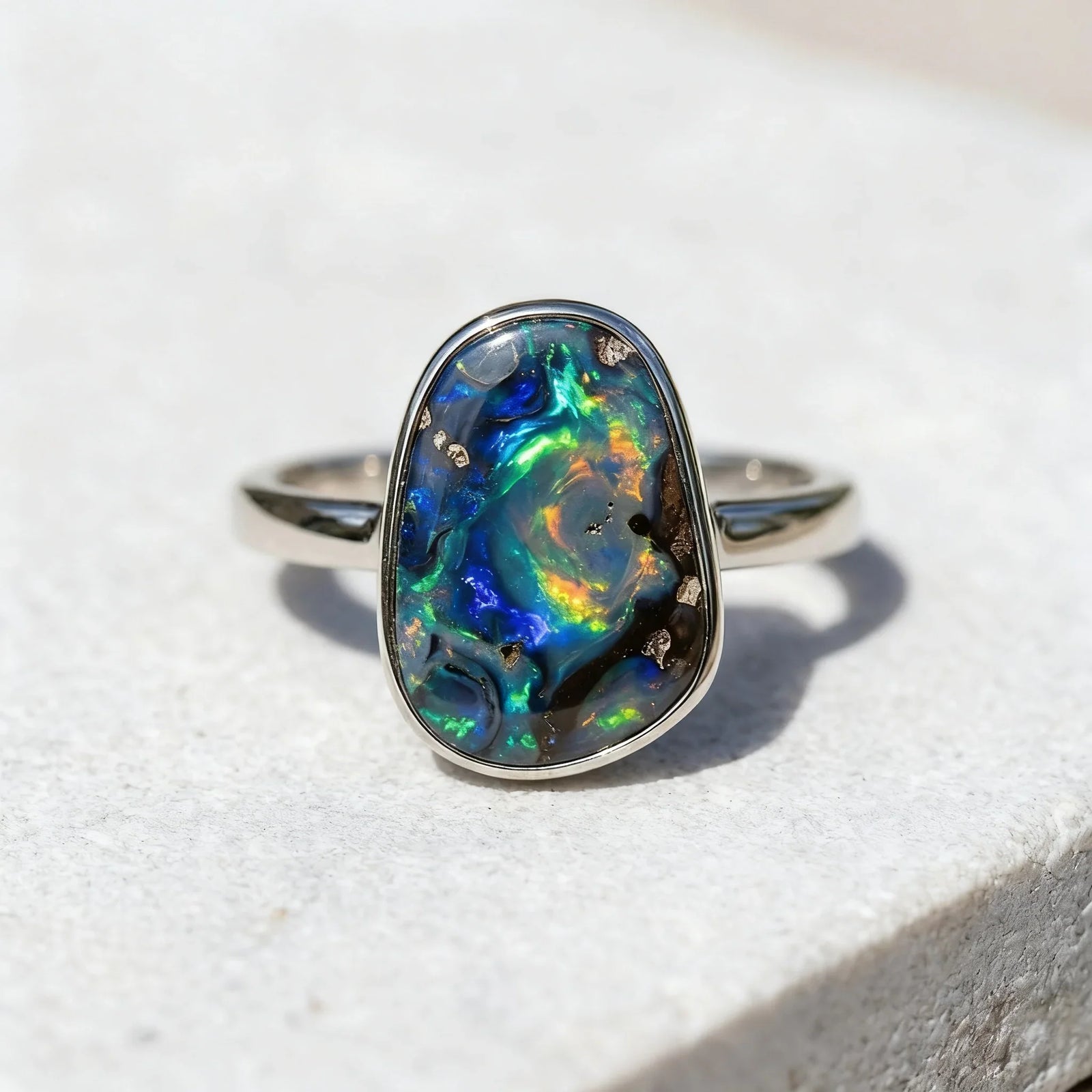 A natural solid black opal ring by Esdomera, showcasing unique and organic flashes of deep blue, green, and orange play-of-color under natural daylight.